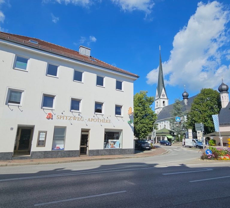 Zentrale Physiotherapie Praxis am Marktplatz 1 in Prien Kathrin Ortinger Naujeck Blick auf das Haus der Spitzwegapotheke in Prien mit Kirche im Hintergrund unter weißblauem strahlenden Himmel