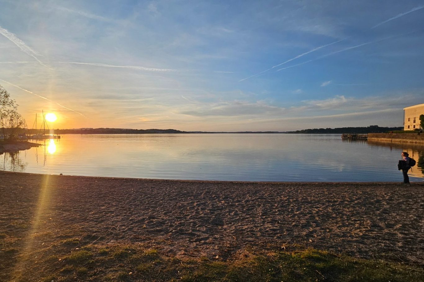Klinik begleitende Physiotherapie Prien Kathrin Ortinger Naujeck Sich im Wasser spiegelnder, rötlich warmer Sonnenuntergang über dem ruhigen Chiemsee mit Blick auf Prien