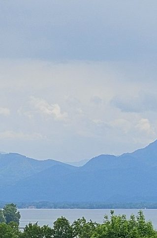 Physiotherapie am Chiemsee in Prien Kathrin Ortinger Naujeck Berglandschaft mit bewölktem Himmel und Chiemsee im Vordergrund.